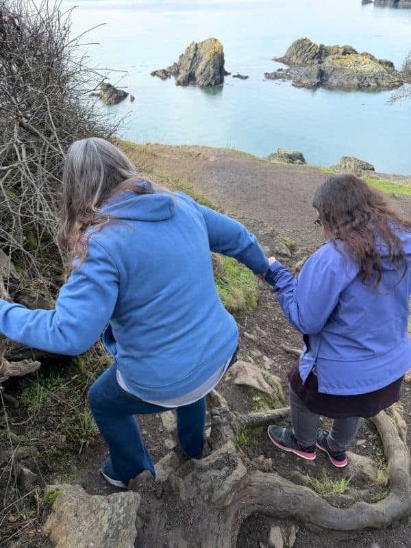 A woman assisting an older woman down a hiking trail at Rosario Head, Washington.