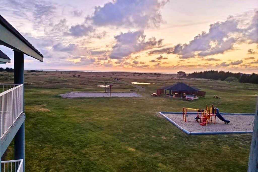 A view from the Breakers Hotel balcony in Long Beach, Washington. There is a grassy field with a trail leading off to the beach and the sunset sky over the Pacific Ocean.