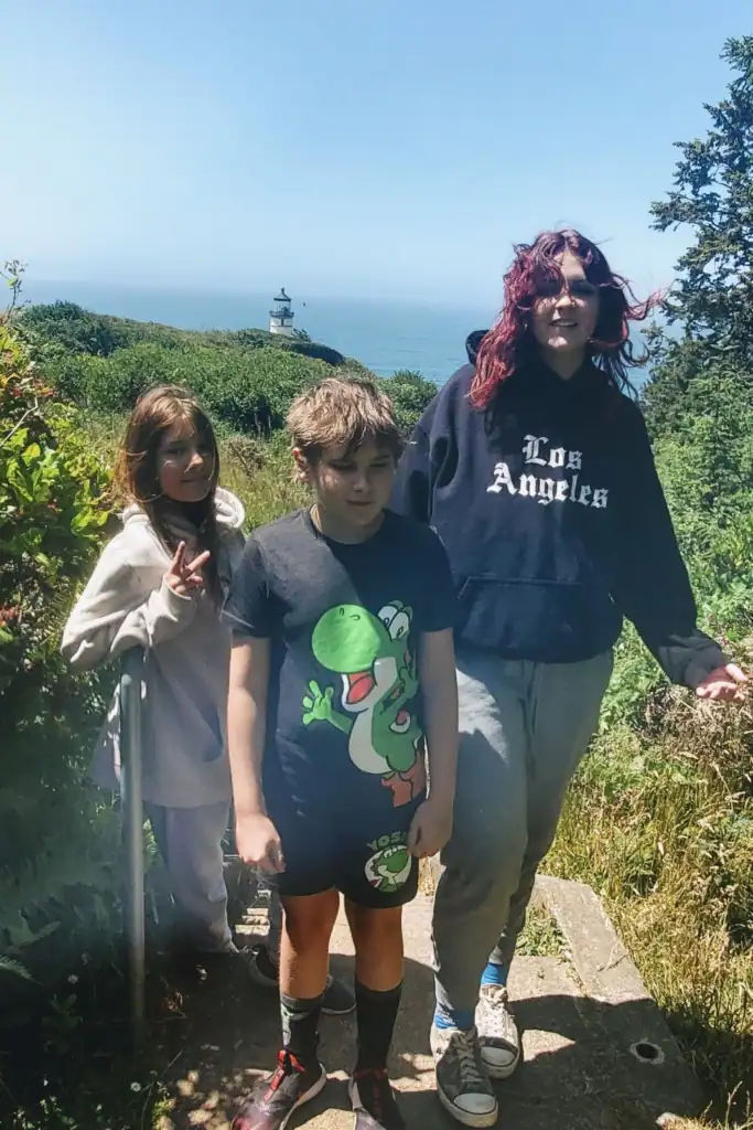 Three kids exploring a coastal trail with a lighthouse in the background near Long Beach, Washington