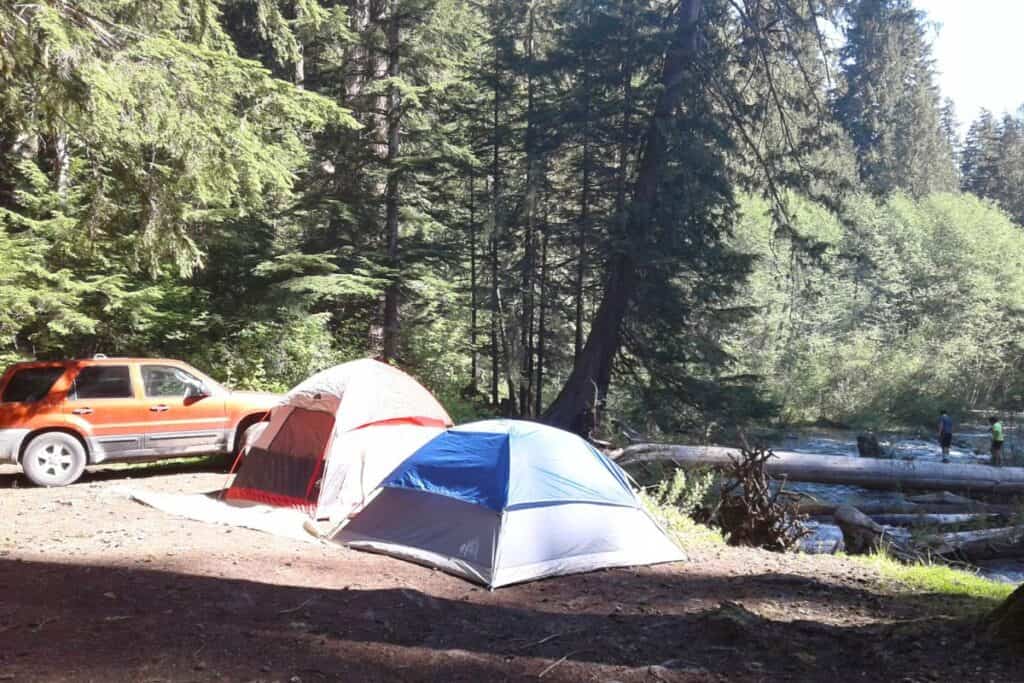 Life in the Pacific Northwest Two tents set up next to a car in the woods, overlooking a river in Greenwater, Washington.