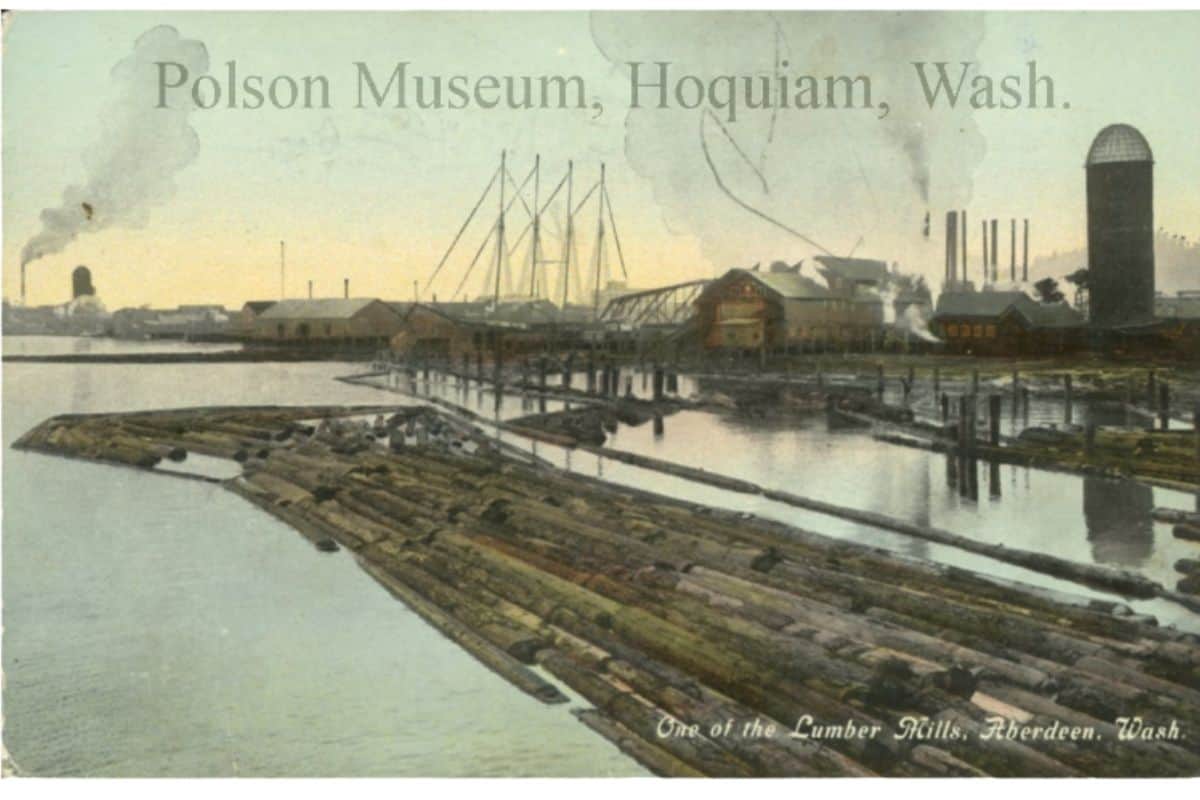 Historic postcard of a Grays Harbor timber mill, courtesy of the Polson Museum in Hoquiam. Vintage colorized postcard from the Polson Museum showing a massive early 1900s lumber mill waterfront in Aberdeen and Hoquiam Washington with thousands of floating logs corralled in the water next to smokestacks and a sailing cargo ship.