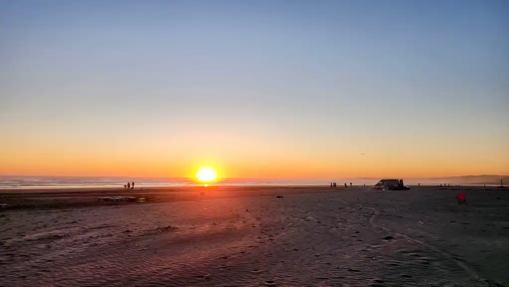 Washington Coast Sunset Beach Escape A wide, sweeping view of a vibrant orange sunset over the vast sandy beach and ocean waves on the Washington Coast.