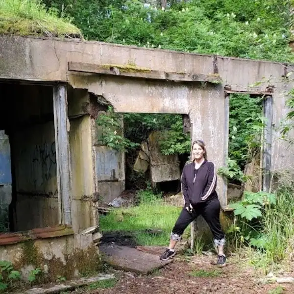 Woman standing beside overgrown concrete ruins in a Pacific Northwest forest