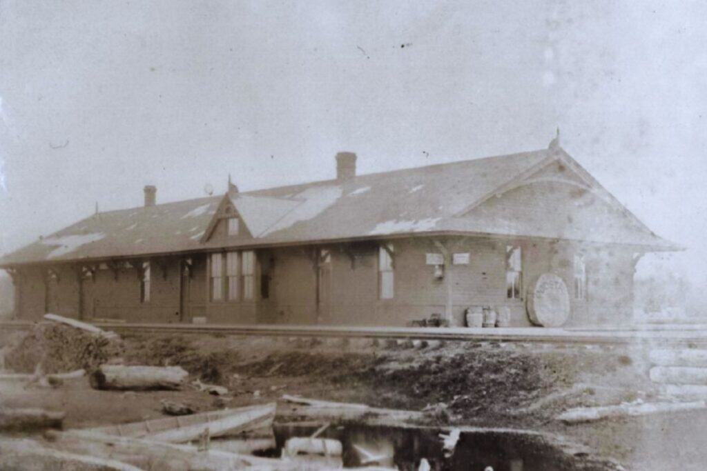 A vintage photograph of the Northern Pacific Railroad depot in Ocosta-by-the-Sea, featuring a large wooden station building and railway tracks.
Photo from Polson Museum, Hoquiam.