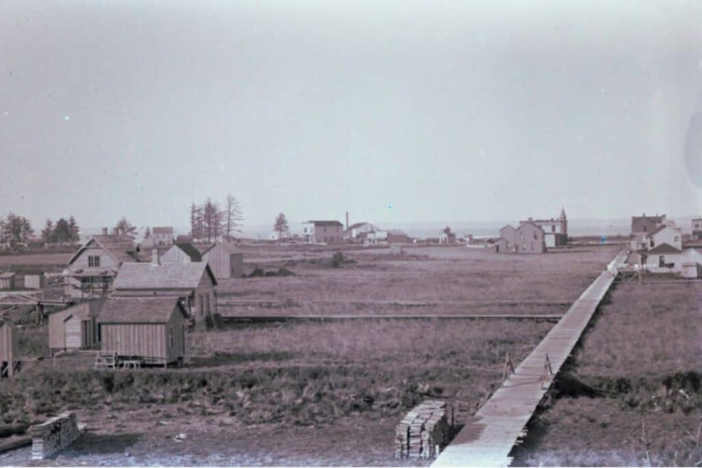 Archival photo of Ocosta-by-the-Sea showing a single-plank boardwalk stretching across an empty field toward distant buildings.