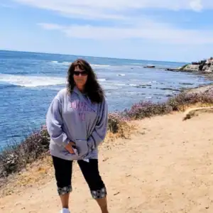 A woman standing on a sandy bluff overlooking the Pacific Ocean.