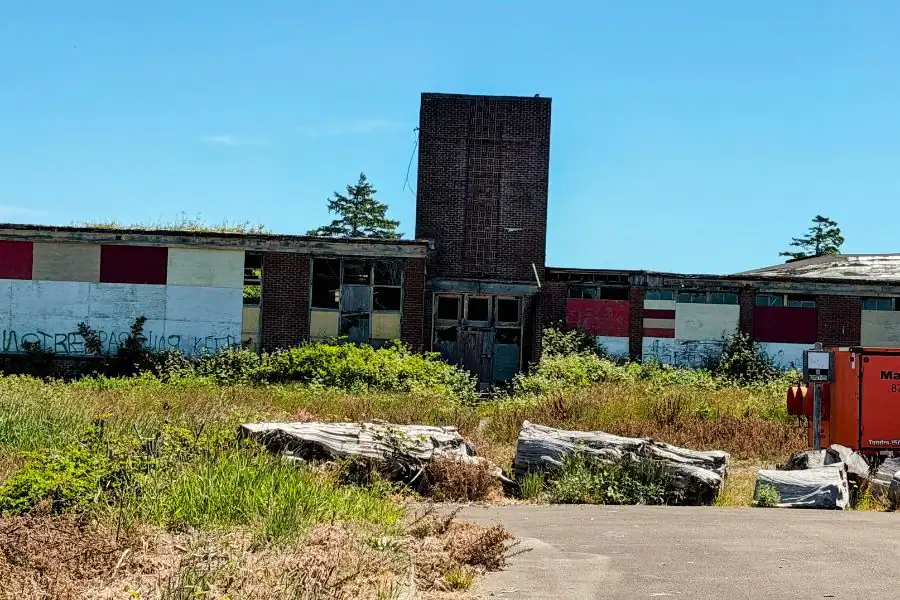 Abandoned old Moclips High School building with boarded windows and overgrown grass in Moclips, Washington.