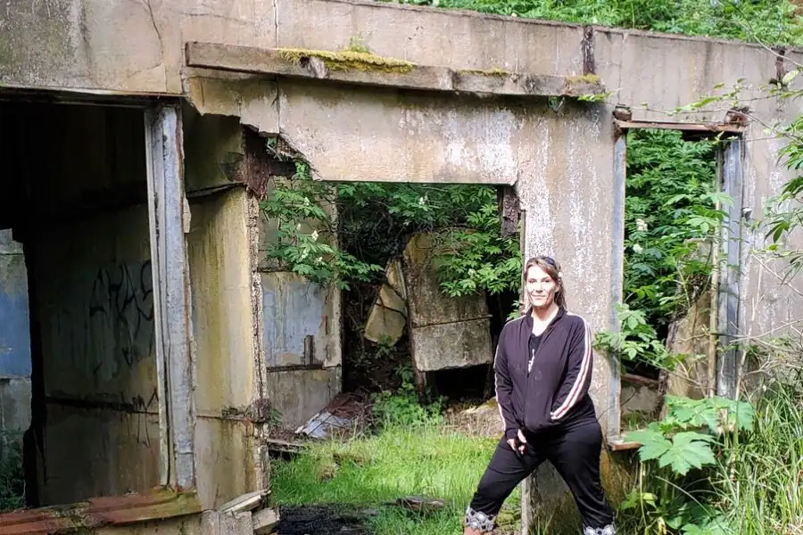 Woman standing beside moss-covered concrete ruins in a Pacific Northwest forest