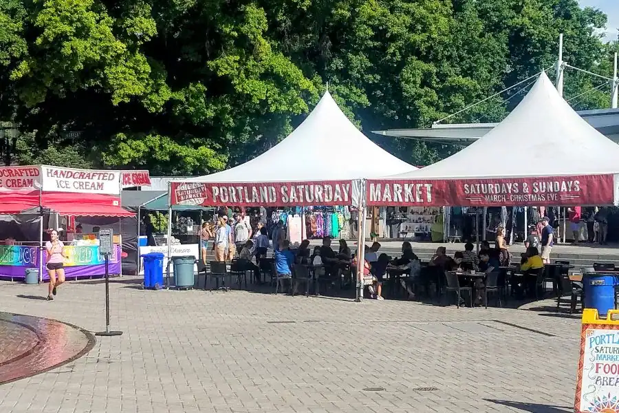 Portland Saturday Market with food vendors, craft booths, and visitors gathered under white tents.