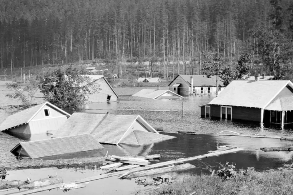 Historic 1915 photograph of houses partially submerged in floodwaters at Rattlesnake Lake, Washington, with a forested hillside in the background.