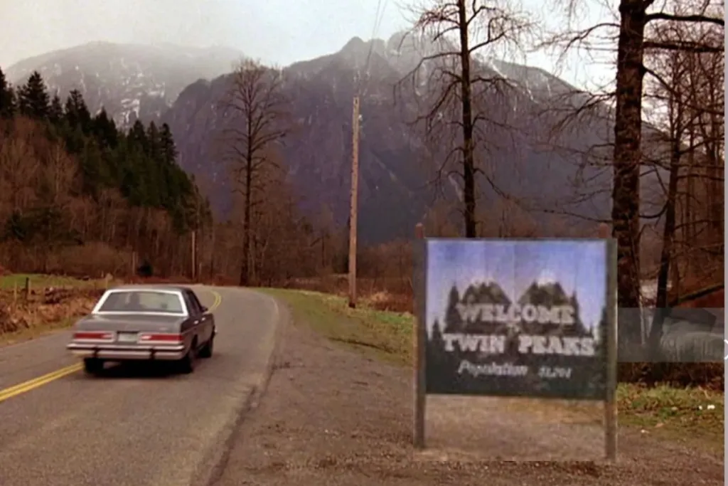 Scene from Twin Peaks showing a car driving along a mountain road past the Welcome to Twin Peaks population sign.